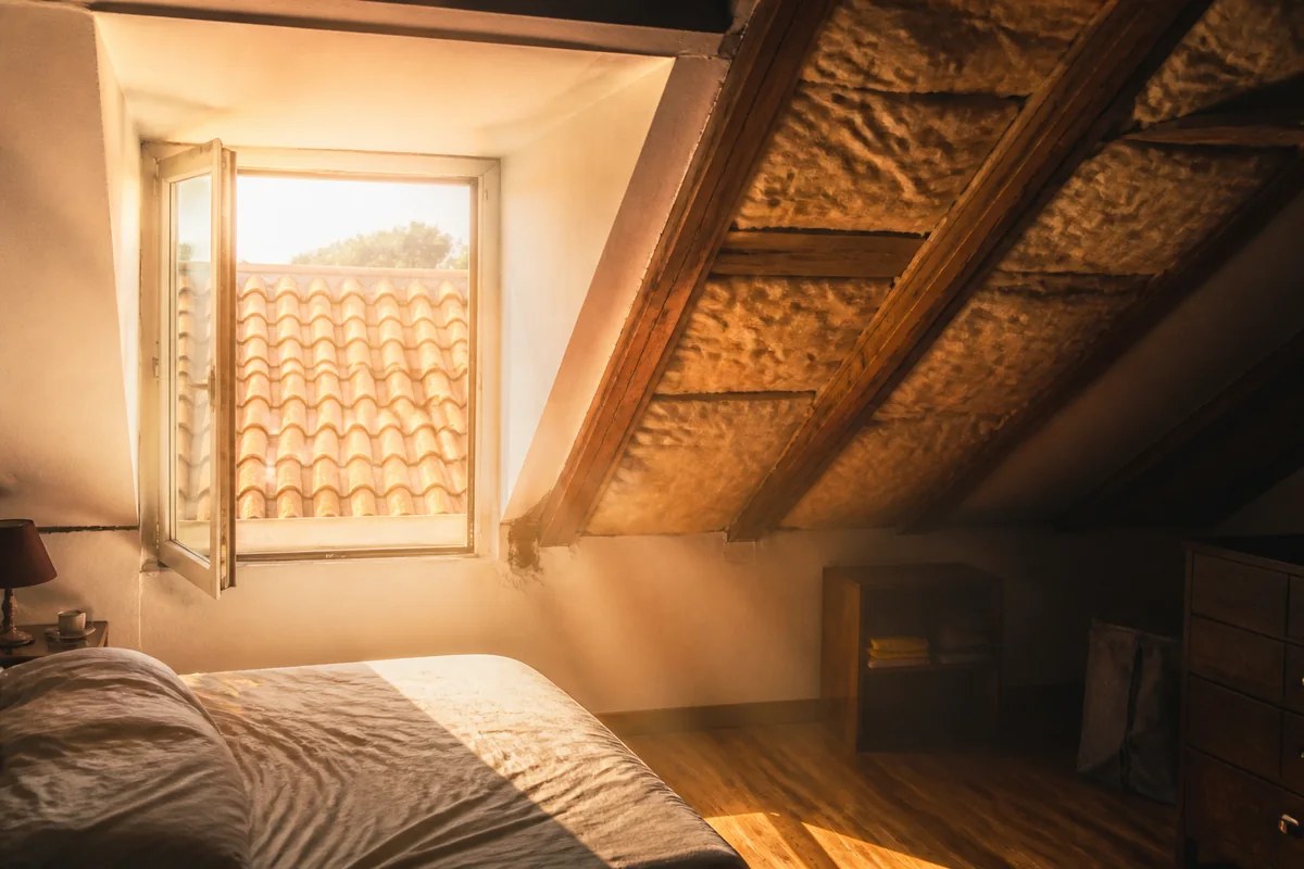 Chambre aménagée sous les combles, très éclairée par une fenêtre de toit, avec la structure de la toiture visible