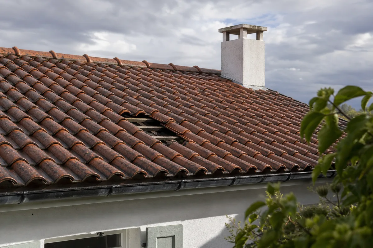 Toiture en tuiles terre cuite avec une ouverture laissée par des tuiles envolées après un orage